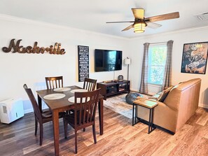 A living room with a dining table, chairs, a sofa, a TV, and a ceiling fan.