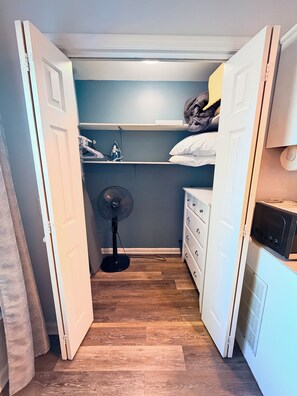 Una habitación pequeña y estrecha con un ventilador, una cama y un aparador blanco.