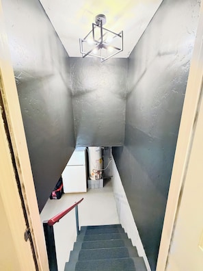 Un escalier étroit menant à une pièce dotée d’un ventilateur de plafond et d’un chauffe-eau.