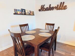 A dining table with four chairs, a wall-mounted shelf with books, and a decorative sign spelling 'Nashville'.