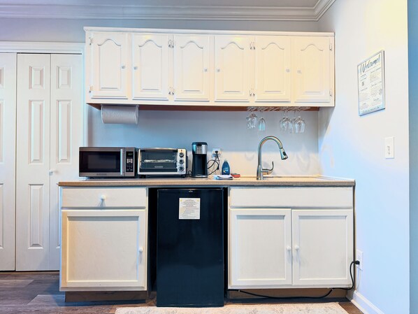 Una cocina con gabinetes blancos, microondas, tostadora, cafetera y lavavajillas.