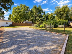 Une allée de gravier mène à une terrasse en bois, qui est entourée d’une clôture en bois et d’arbres.