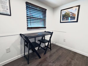 A small dining area with a table and chairs, a window with blinds, and a framed picture on the wall.