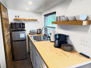 Eine kompakte Küche mit Kühlschrank, Mikrowelle, Toaster, Wasserkocher und Kaffeemaschine.