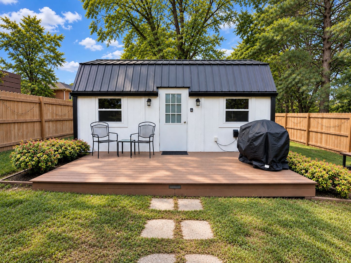 A small house with a deck, two chairs, and a barbecue grill.