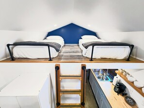 A compact room with two beds, a kitchenette, and a small wooden ladder.