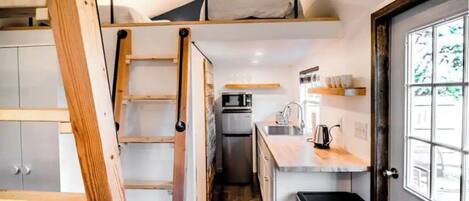 Cocina compacta con cama tipo litera, microondas y lavamanos.