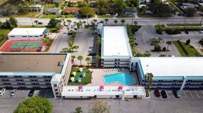 Relax by the pool surrounded by sun loungers and umbrellas, with a tennis court and parking nearby.