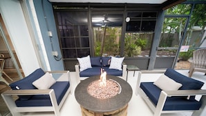 Un foyer extérieur circulaire en pierre, avec un canapé bleu et des coussins placés devant.