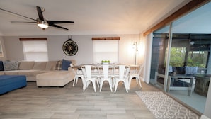 Un salon moderne avec un coin repas, doté d’un ventilateur de plafond, d’une horloge et de grandes fenêtres.