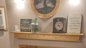 Uma lareira com prateleira, exibindo objetos decorativos, um relógio fixado na parede e uma silhueta de árvore emoldurada.