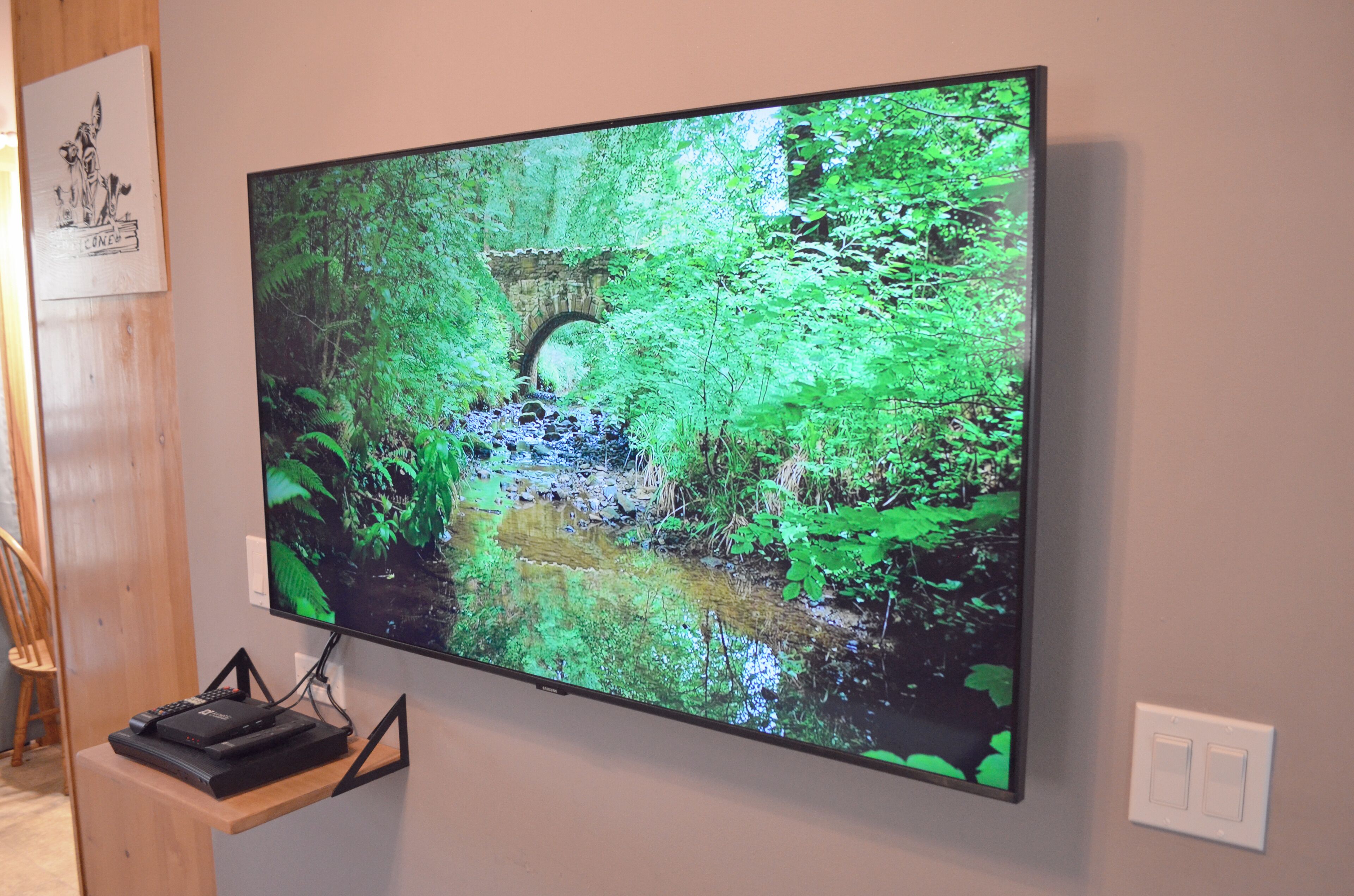 Un televisor de pantalla plana montado en la pared mostrando una exuberante escena de bosque verde.