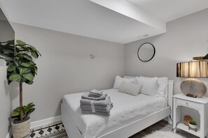 A neatly arranged bedroom with a bed, a bedside lamp, a small potted plant, and a wall-mounted mirror. - Cozy Modern Beautiful Studio+Parking. Walk to DC Metro. Perfect for Long Stays! (Washington)
