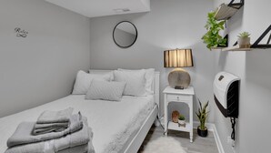 A modern bedroom with a bed, a bedside table with a lamp, a mirror, and a shelf with plants. - Cozy Modern Beautiful Studio+Parking. Walk to DC Metro. Perfect for Long Stays! (Washington)