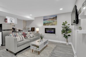 A modern living room with a grey sofa, white coffee table, and a painting of a lake. - Cozy Modern Beautiful Studio+Parking. Walk to DC Metro. Perfect for Long Stays! (Washington)