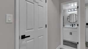A hallway leading to a bathroom with a white door labeled "Closet," a round mirror, and a white sink with black handles. - Cozy Modern Beautiful Studio+Parking. Walk to DC Metro. Perfect for Long Stays! (Washington)