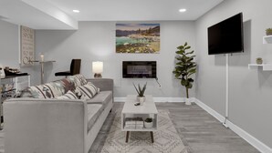 A modern living room with a grey sofa, a white coffee table, a flat-screen TV mounted on the wall, and a large landscape painting above the TV. - Cozy Modern Beautiful Studio+Parking. Walk to DC Metro. Perfect for Long Stays! (Washington)