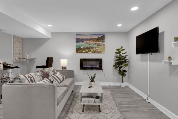 A modern living room with a grey sofa, a white coffee table, a flat-screen TV mounted on the wall, and a large landscape painting above the TV. - Cozy Modern Beautiful Studio+Parking. Walk to DC Metro. Perfect for Long Stays! (Washington)