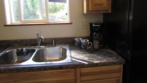 A kitchen with a double sink, wooden cabinets, a coffee maker, and two mugs on the counter. - Peaceful Talkeetna Getaway 4 (Talkeetna)