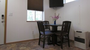 A dining area with a table, four chairs, a vase with flowers, a wall-mounted TV, and a standing heater. - Peaceful Talkeetna Getaway 4 (Talkeetna)