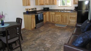 A kitchen with wooden cabinets, a stove, a refrigerator, and a dining area with a table and chairs. - Peaceful Talkeetna Getaway 4 (Talkeetna)