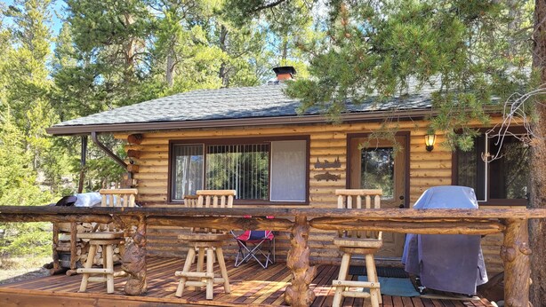 Une cabane en rondins dotée d’une terrasse, d’un espace salon extérieur et d’un barbecue.