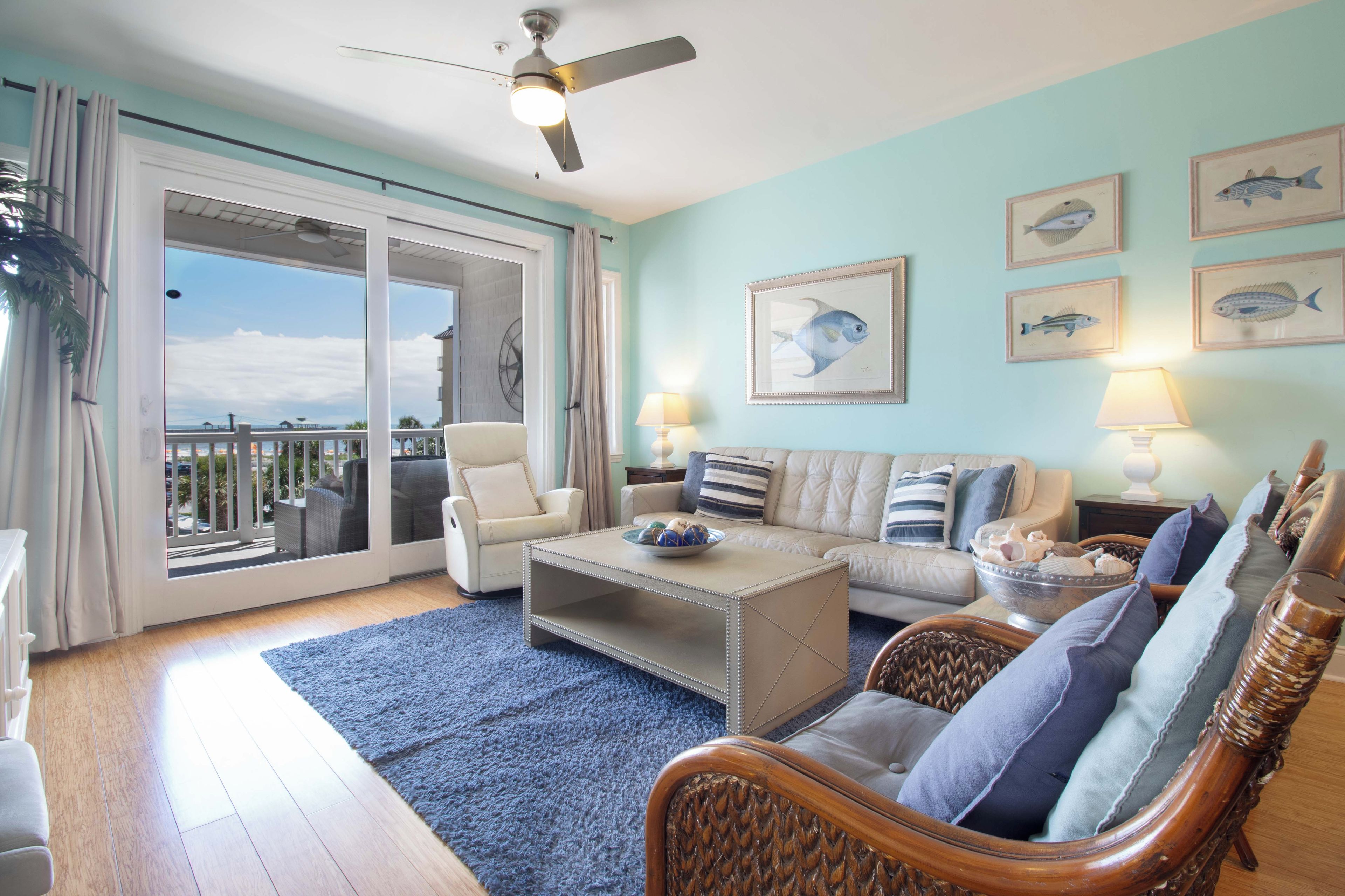A spacious living room with a balcony, a ceiling fan, and multiple framed fish paintings on the wall.