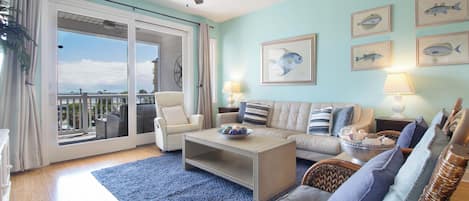 A spacious living room with a balcony, a ceiling fan, and multiple framed fish paintings on the wall.
