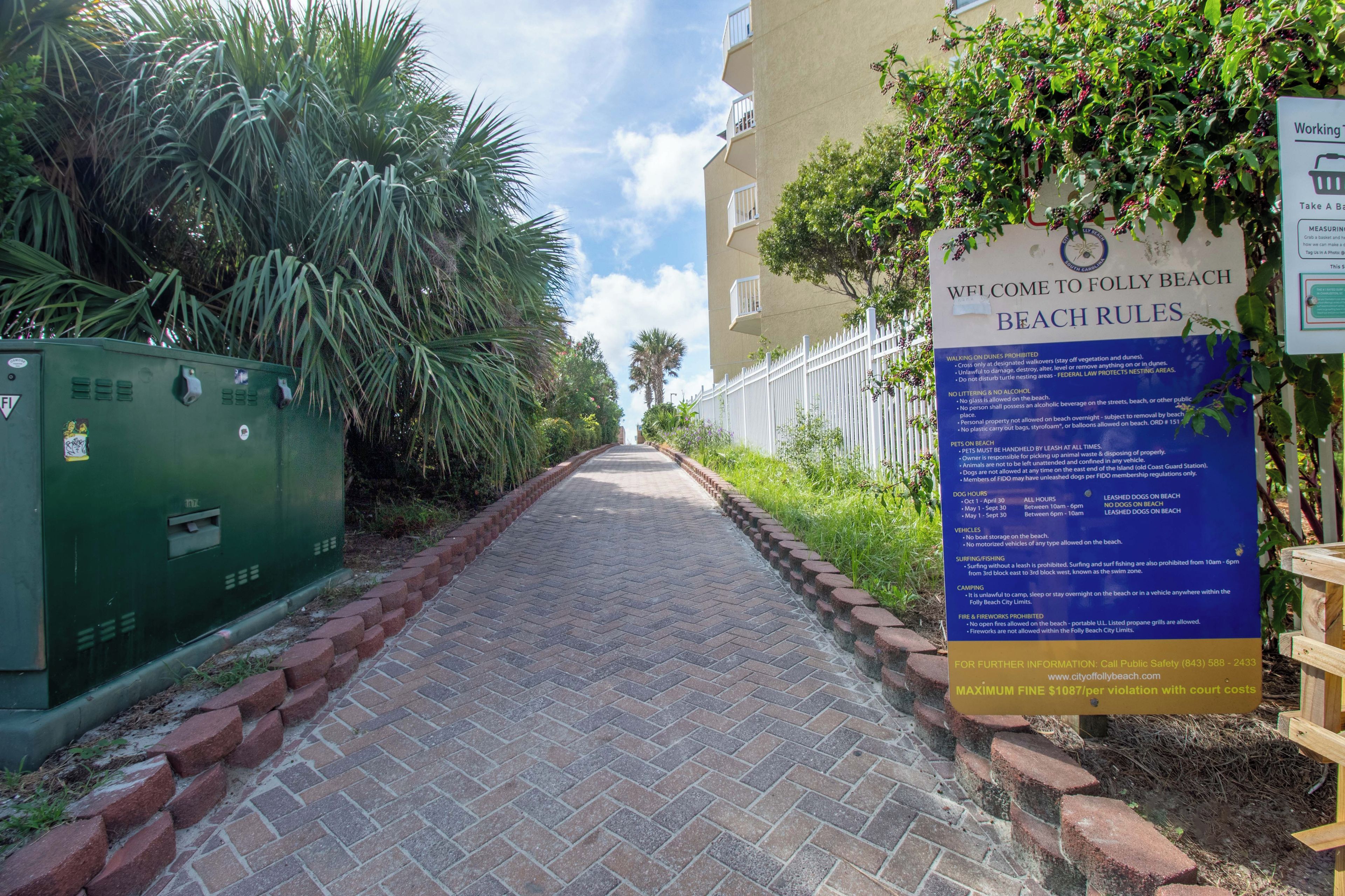 A paved pathway leading to a building with a signboard displaying beach rules.
