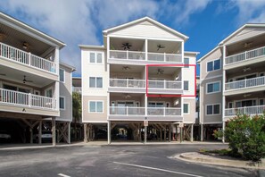 A multi-story residential building with balconies, a parking area, and a clear sky.