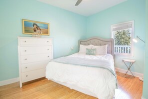 A bedroom with a bed, dresser, window, and a painting on the wall.