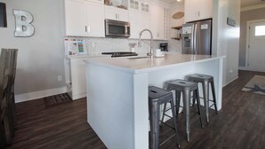 A modern kitchen with white cabinetry, a large island with stools, stainless steel appliances, and a welcome sign. - Across from the beach luxury~ Folly Beach Stay (Folly Beach)