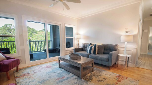 A living room with a sofa, coffee table, and a view of a balcony. - The Perfect 30 Day Escape! ~ My Getaway Home (Charleston)
