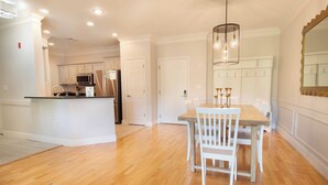 A spacious kitchen with white cabinets, a central island, and a dining area with a wooden table and white chairs. - The Perfect 30 Day Escape! ~ My Getaway Home (Charleston)