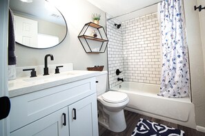 A bathroom with a white sink, black faucets, a white toilet, a shower with a white curtain, and a mirror. - Cozy home a mile from downtown. (Prescott)