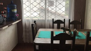 Een eetgedeelte met een tafel voor twee personen, stoelen, een waterdispenser en een uitzicht door een raam met een rasterwerkontwerp.