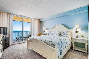 Relax in this serene hotel room with a large bed, television, and sliding glass door leading to a balcony with ocean views.
