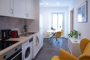 Une cuisine compacte dotée d’appareils électroménagers modernes, un coin repas avec des chaises jaunes et une vue sur l’extérieur.