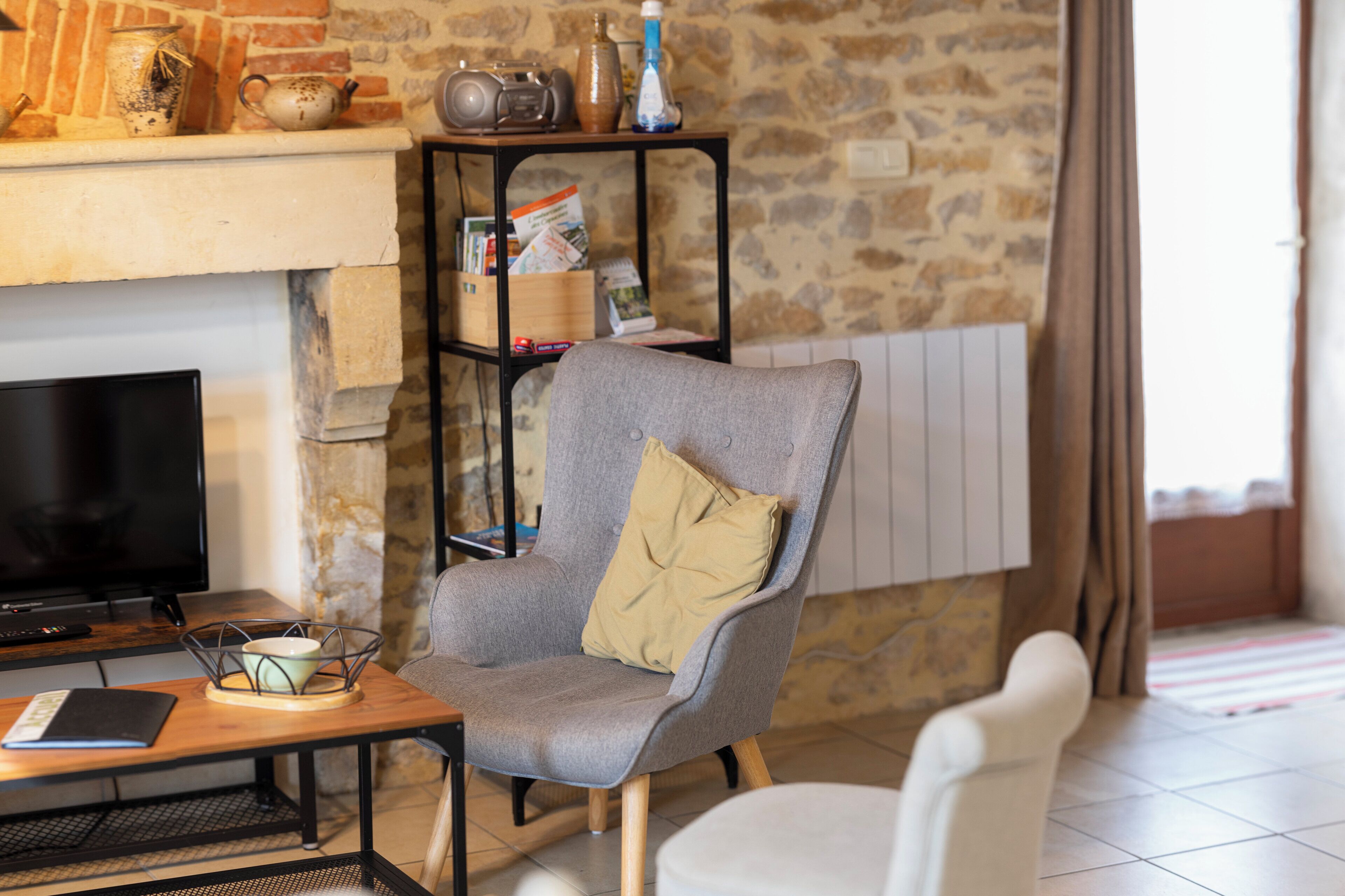 Ein Wohnzimmer mit Steinsandsteinwand, Kamin, Fernseher, grauem Sessel mit Kissen, Holzbeistelltisch und einem schwarzen Bücherregal.
