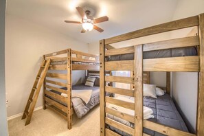 Quarto com duas beliches, um ventilador de teto e uma porta.