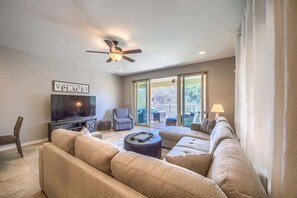 A living room with a sofa, ottoman, TV, ceiling fan, and a sign that reads 'Welcome to our place.'