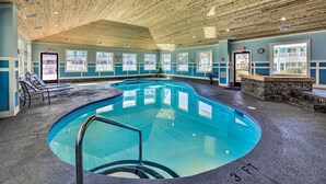 Un'ampia piscina interna con soffitto in legno, pareti blu e un'area relax con panche in pietra.