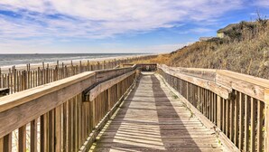 Una passerella di legno che conduce a una spiaggia, con una recinzione di legno su un lato e un edificio sull'altro.