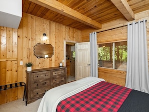 A wooden cabin bedroom with a bed, dresser, and a mirror on the wall.