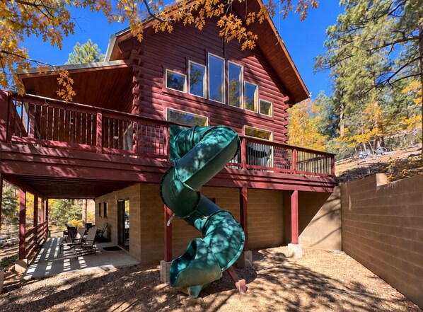 A log cabin with a spiral staircase, a covered patio, and a view of a forested area. - Family Fun Log Cabin in the Pines - Game Room + Firepit  + Slide (Prescott)