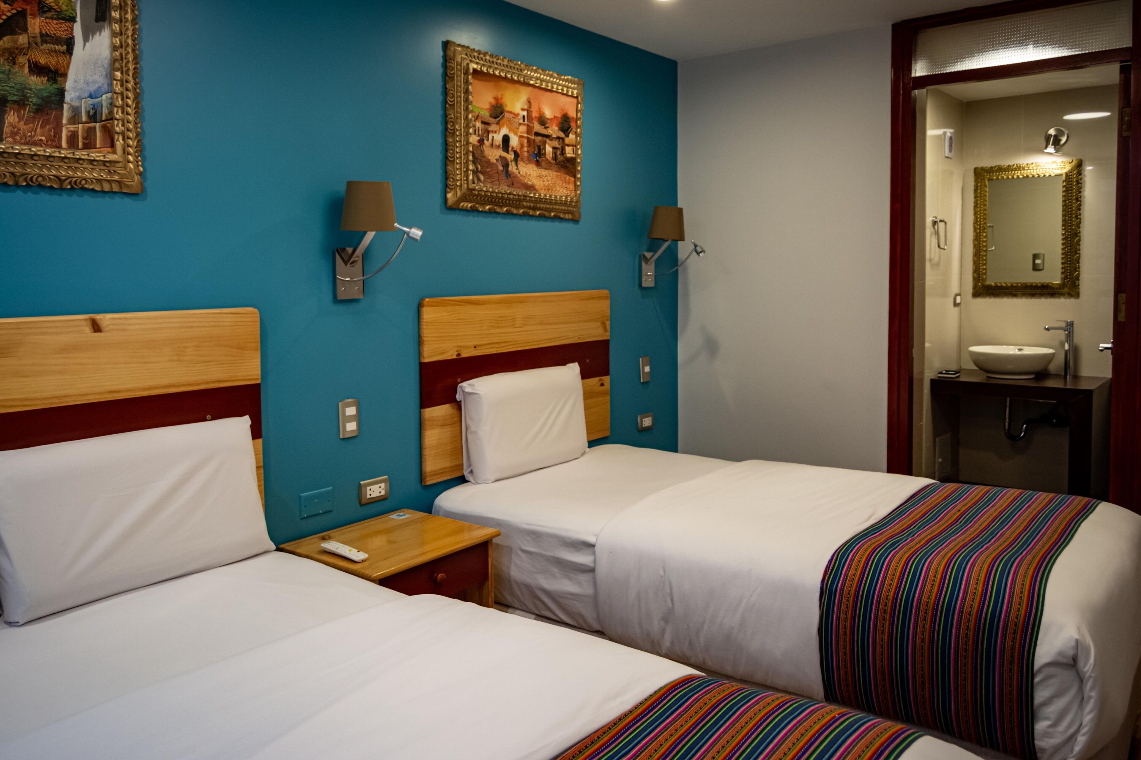A hotel room with two beds, a bathroom with a mirror and sink, and a painting on the wall.