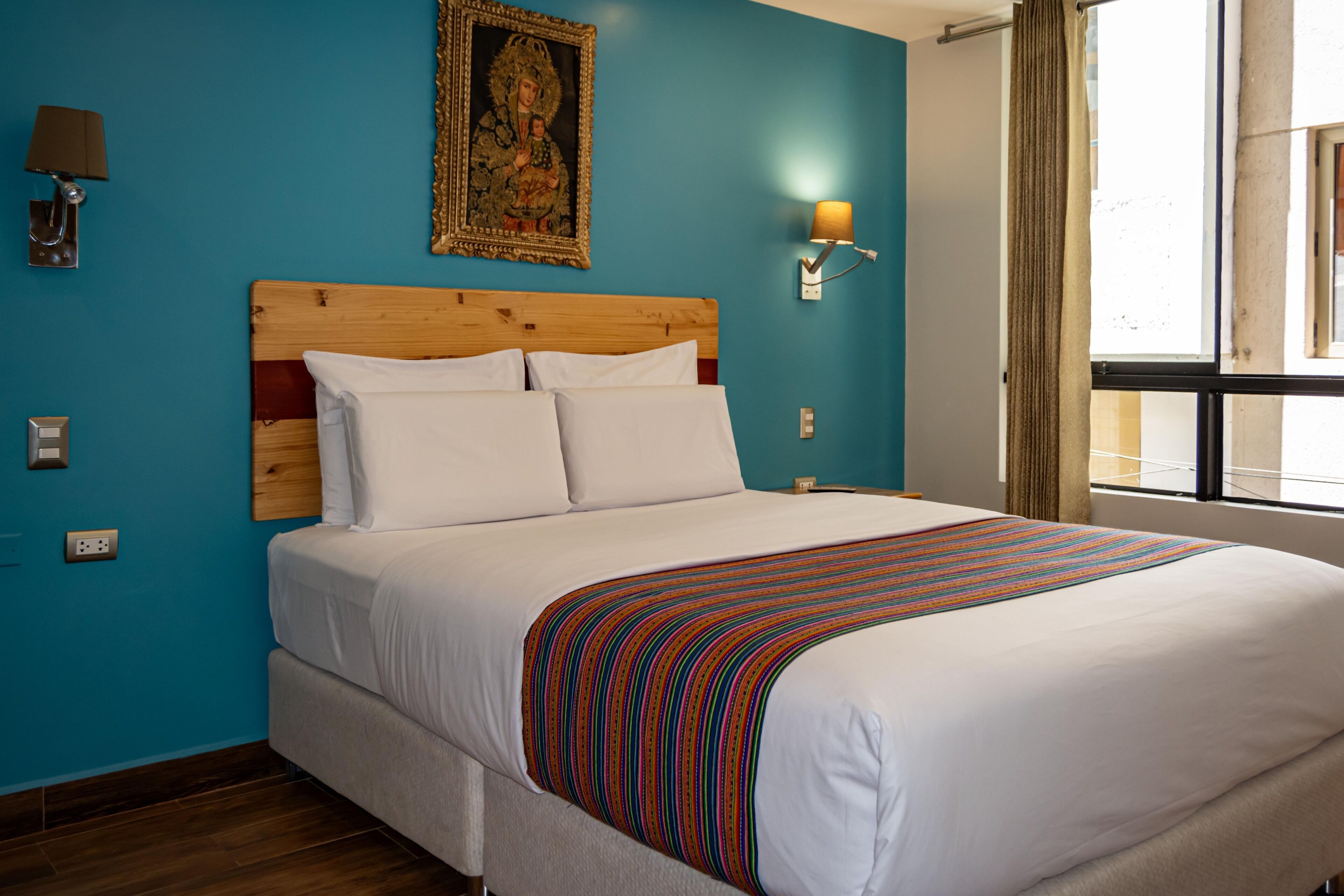 Hotelkamer met een groot bed, een houten hoofdbord, een blauwe muur, een inlijsting afbeelding, een lamp en een raam met gordijnen.