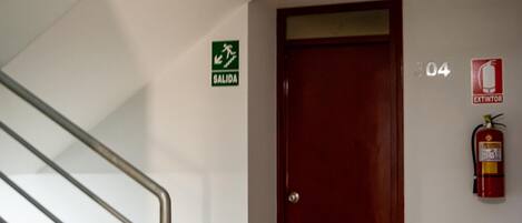 Escada com corrimão metálico que leva a um piso de madeira. Uma porta vermelha com o número