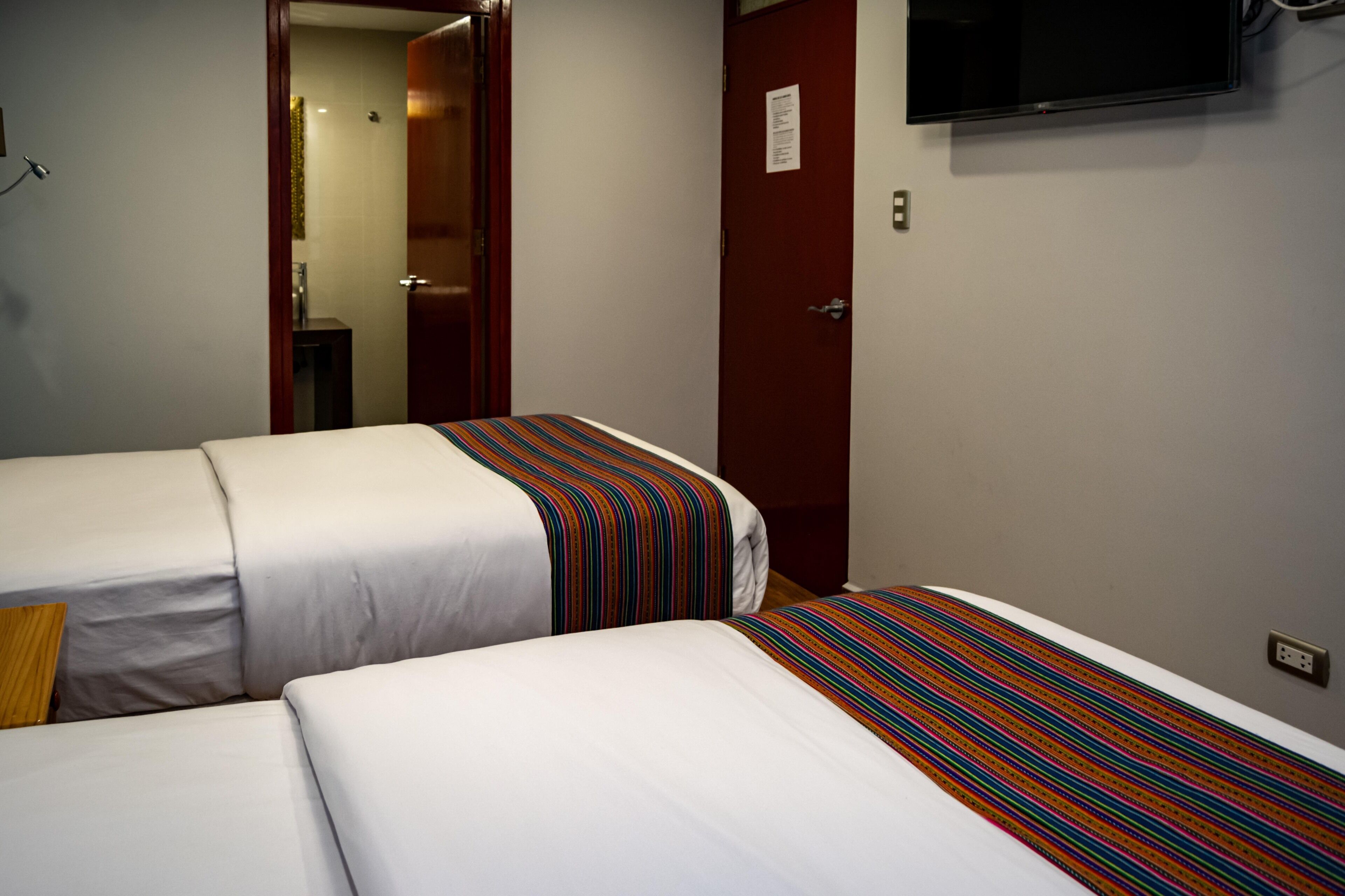A hotel room with two beds, a TV mounted on the wall, and a door with a sign.