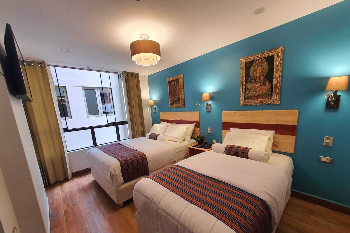A hotel room with two beds, a large window, and artwork on the walls.